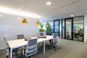 Modern vergaderruimte op Johan Huizingalaan met een witte tafel, ergonomische stoelen, hanglampen en zicht op een glazen kantoorruimte.